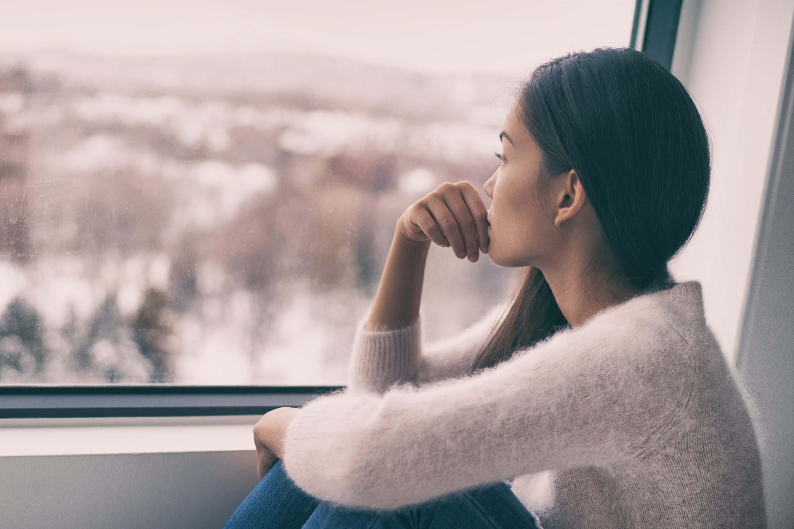 Winter depression - seasonal affective disorder mental health woman sad comtemplative looking out the window alone.